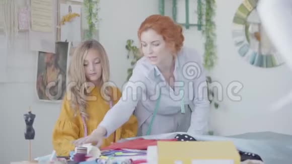 红发的母亲和她的女儿欣赏一块漂亮的布料裁缝在车间工作快乐的爱视频的预览图