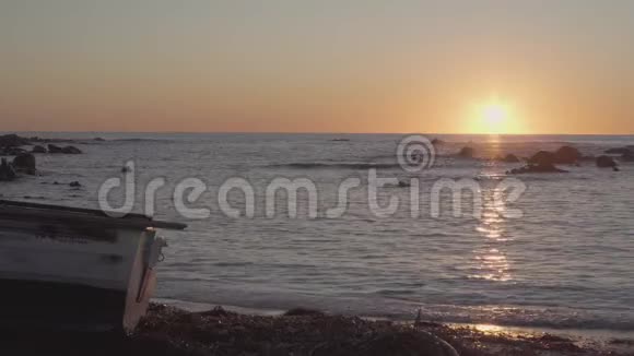 黎明或黄昏时分沙滩上的木船海面上有小浪水面上有太阳的倒影视频的预览图