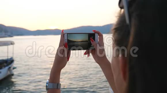 女人在他的智能手机上用金色日落拍摄风景优美的海洋景观女孩用手机变漂亮视频的预览图