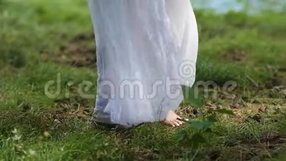 光着脚的女孩穿着白色的裙子走在绿草上视频的预览图