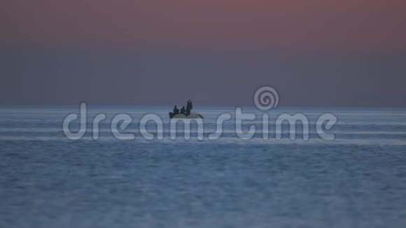 一队渔民在一张网上工作在海上的一艘船上捕鱼以观赏粉红色的日落视频的预览图