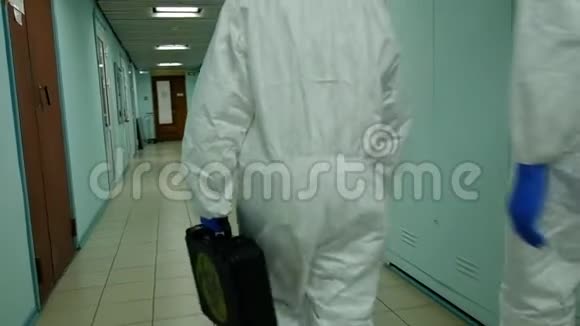 两位穿着病毒保护服和口罩的病毒学家正拿着一个手提箱沿着走廊走去后视镜视频的预览图