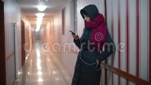 穿夹克的女孩在旅馆的走廊里用智能手机视频的预览图