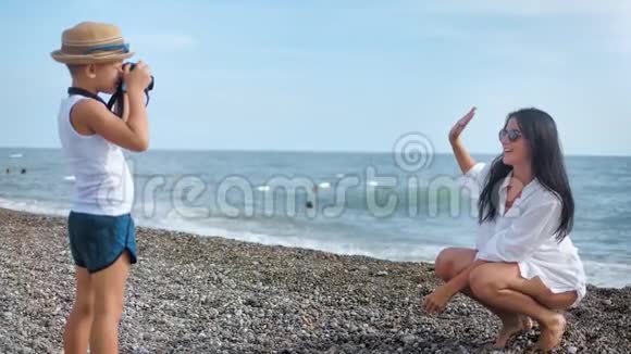 在男孩用相机拍照时在海滩上摆姿势拍照的免费旅游妇女视频的预览图