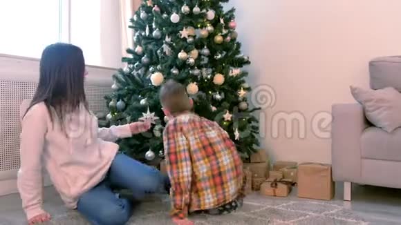 妈妈和儿子看着家里坐在圣诞树附近的圣诞玩具视频的预览图