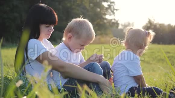 快乐的年轻爱妈妈和她的小儿子和女儿在感情上并在大自然中玩得开心一家人坐在一个清澈的地方视频的预览图