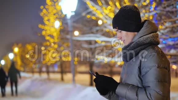一个十几岁的孩子在雪夜街使用智能手机视频的预览图