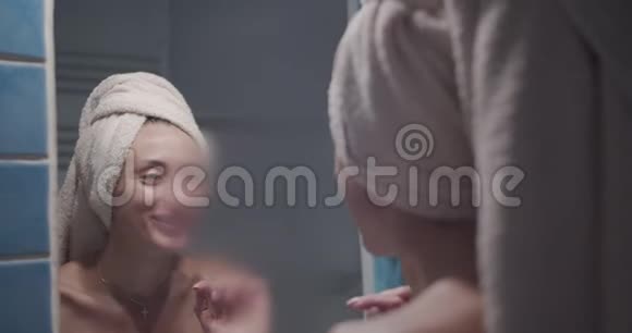 年轻的成年女子在雾状浴室擦镜子玻璃女孩裹着白毛巾微笑着视频的预览图