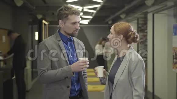 两个白人同事休息时在空地办公室聊天男人和女人拿着咖啡杯讨论视频的预览图