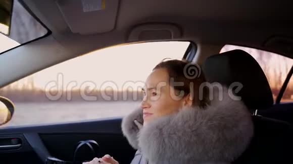 一个穿着温暖的银色夹克带毛皮领子的女人坐在汽车的前乘客座位上从侧面射击视频的预览图