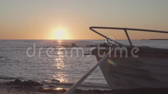黎明或黄昏时分沙滩上的木船海面上有小浪水面上有太阳的倒影视频的预览图
