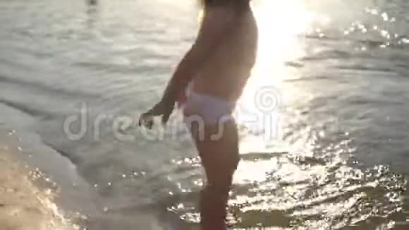 宝宝在水中飞溅泼水可爱的孩子在海滩上快乐地玩耍快乐的孩子在日落时洗澡视频的预览图