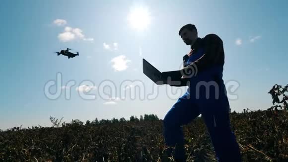 农业工人正在用一台笔记本电脑和一架无人机在附近飞行视频的预览图