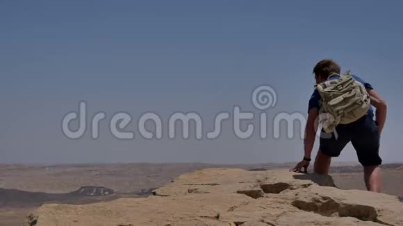 年轻男子背着背包坐在悬崖边看着沙漠视频的预览图