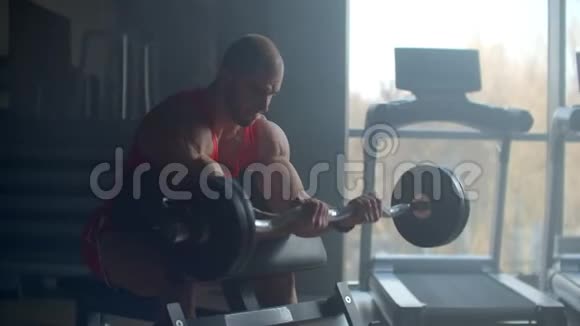 健美男子在健身房的长凳上做二头肌起重杠铃视频的预览图