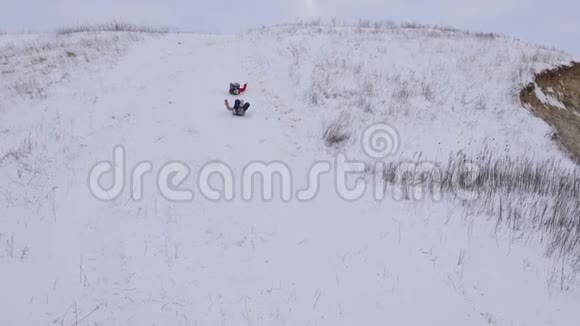 圣诞节期间快乐的孩子们在冬天的公园里从雪山上滑过雪橇慢动作视频的预览图
