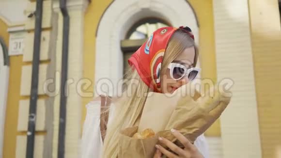 站在街上的一个积极的漂亮年轻女人嗅着刚出炉的面包和牛角面包时尚迷人视频的预览图