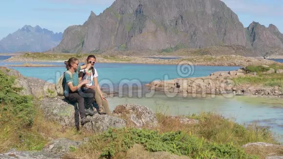 两个年轻的女旅行者坐在岩石上从瓶子里喝水视频的预览图