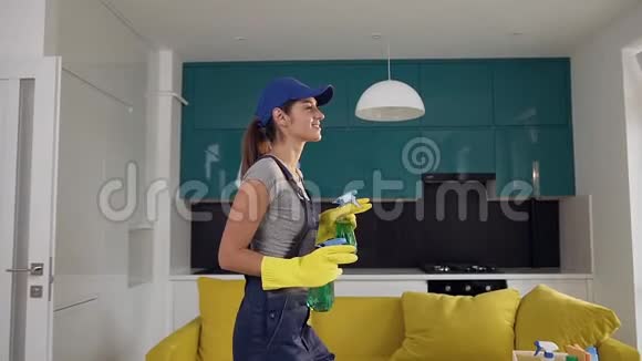 30多岁的漂亮女孩穿着制服拿着两瓶洗涤剂喷洒它们在厨房里跳舞视频的预览图
