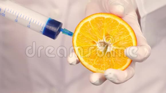 特写镜头医生戴着白色医疗手套拿着半个橙色用注射器注入一些蓝色液体视频的预览图