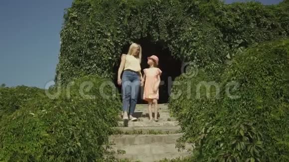 妈妈和女儿下楼梯可爱的金发母亲和女儿在夏天的花园或公园里牵手散步视频的预览图