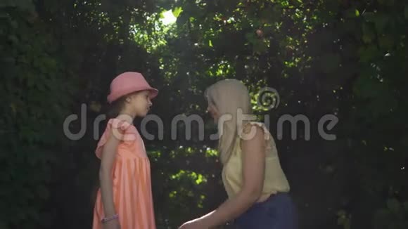 可爱的母亲和她的女儿一起在夏天的花园或公园里度过时光女人亲吻女孩的手视频的预览图