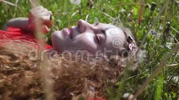卷曲迷人的女孩躺在绿草上年轻漂亮的女人闭上了眼睛穿红色T恤的快乐女士视频的预览图