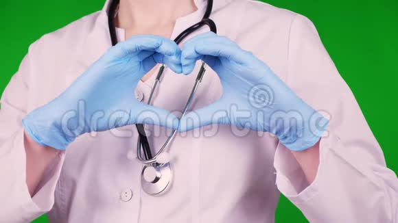 特写镜头医生穿着白色医疗制服带着听诊器戴着蓝色医疗手套手握心形手掌视频的预览图