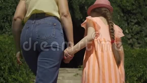 妈妈和女儿爬楼梯可爱的金发母亲和女儿在夏天的花园或公园里牵手散步视频的预览图