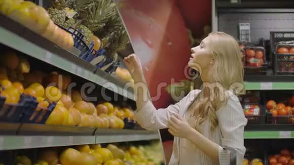 女人选择一个菠萝水果并把它放在购物篮里拿小菠萝躺在附近女性客户视频的预览图