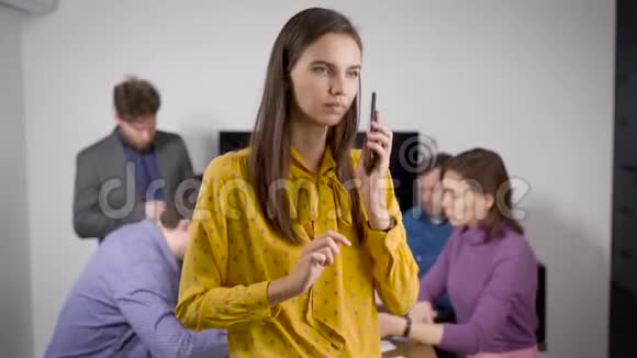 年轻的黑发女子正用手机在办公室会议室交谈工人们正在后台工作视频的预览图