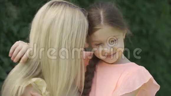 妈妈吻她小女儿的肖像可爱的金发母亲和她的小女儿在夏天公园拥抱快乐视频的预览图