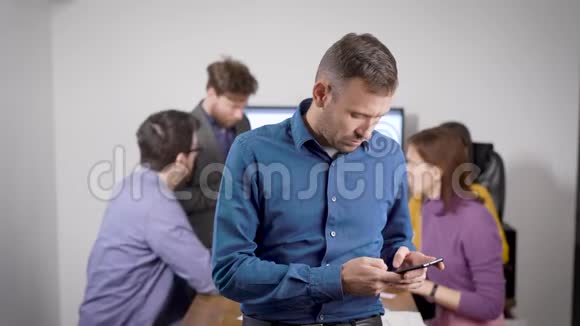 男人在智能手机上打短信站在办公室会议室商务人士在交流视频的预览图