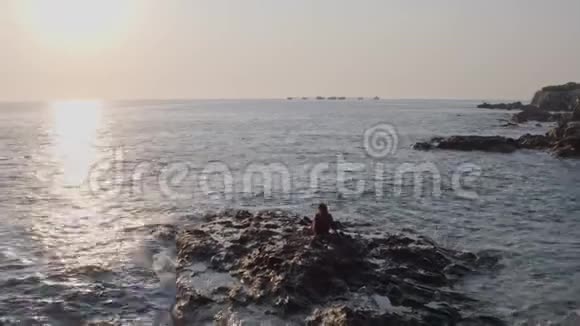 无人机飞行一个女孩坐在岩石海岬上看着大海视频的预览图