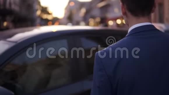 慢动作的年轻人坐在街上的黑色汽车里穿着优雅蓝色西装的微笑商人打开了门视频的预览图