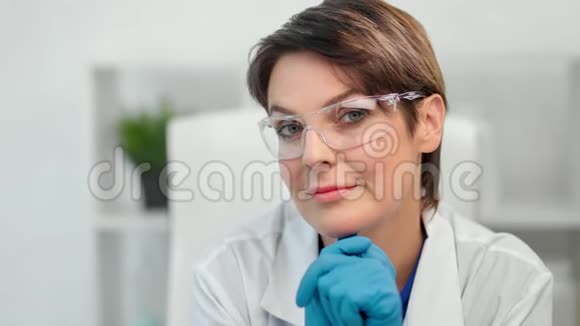 戴着眼镜白大褂戴着手套的美丽成熟女科学家的笑脸视频的预览图
