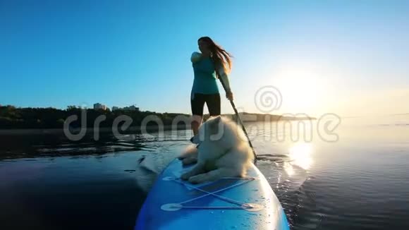 一位女士和她的狗骑着桨板的正面景色视频的预览图