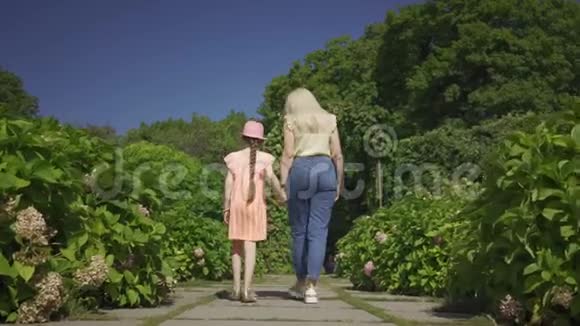 后景可爱的金发妈妈和小可爱的女儿在夏天的花园里牵手散步幸福家庭视频的预览图