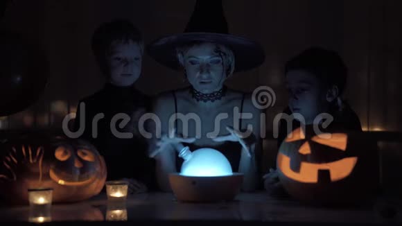 妈妈和两个儿子在万圣节扮演女巫晚上桌子上有一盏神奇的灯和一个南瓜视频的预览图