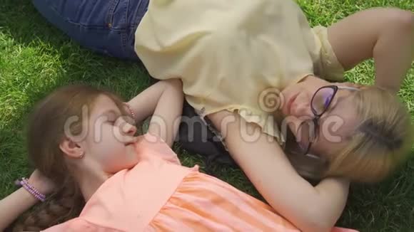 可爱的金发母亲和她可爱的女儿躺在夏天的花园或公园的草地上家庭幸福妇女与妇女视频的预览图
