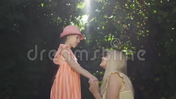 漂亮的母亲和她的女儿一起在夏天的花园或公园里度过时光女人亲吻女孩的手视频的预览图