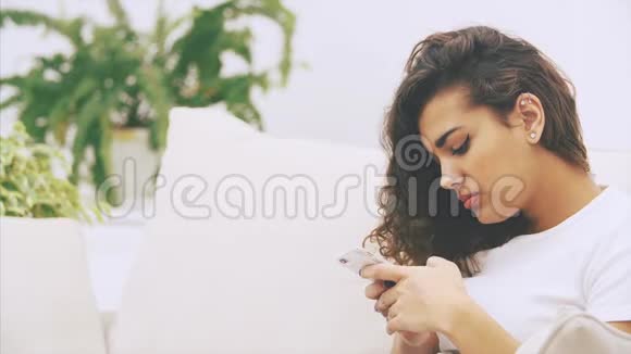 可爱古怪的美国黑人女孩坐在沙发上手里拿着电话看上去又病又累她头痛视频的预览图