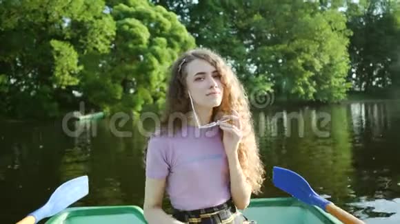 迷人的卷发女孩坐在船上微笑穿着紫色t恤的快乐年轻女子手拿眼镜视频的预览图