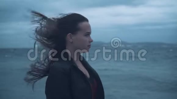 暴风雨中海边一个穿着自行车夹克的长发女孩的肖像阴天又冷大海在暴风雨中视频的预览图