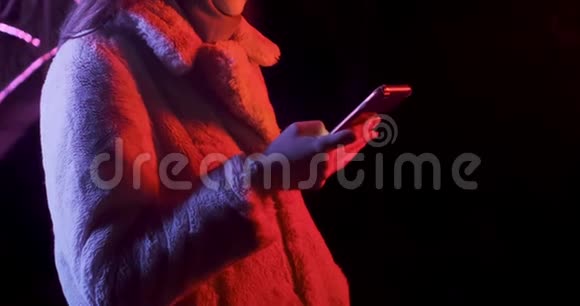 漂亮的黑发女人穿着红色和蓝色霓虹灯在晚上看智能手机时尚模特女孩化妆和视频的预览图