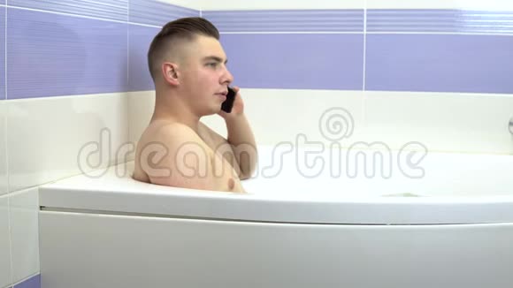 一个年轻人躺在浴缸里打电话一个男人在洗澡时放松视频的预览图