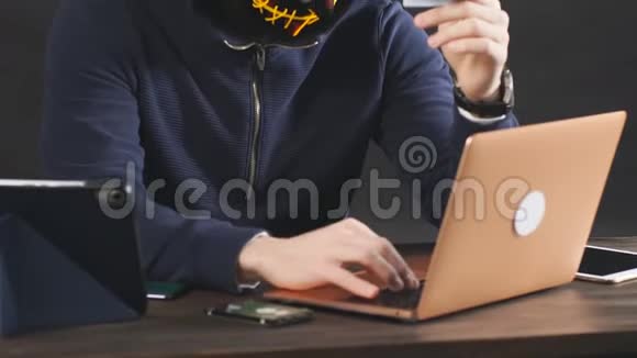 蒙面黑客用笔记本电脑在黑暗的办公室里访问信用卡视频的预览图