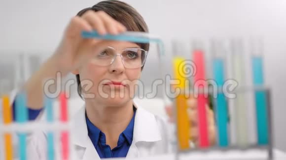 聚焦成熟女化验员在安全眼镜中混合彩色试剂管制作研究视频的预览图