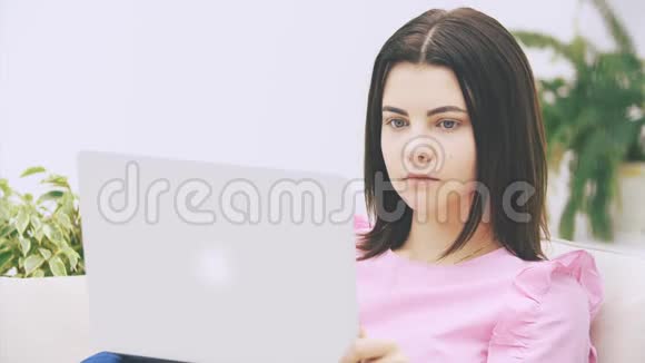 可爱的白种人黑发女孩坐在沙发上手提电脑上网冲浪看起来很集中而且视频的预览图