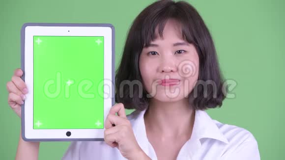 一位快乐的亚洲女商人在展示数码平板电脑时说话视频的预览图